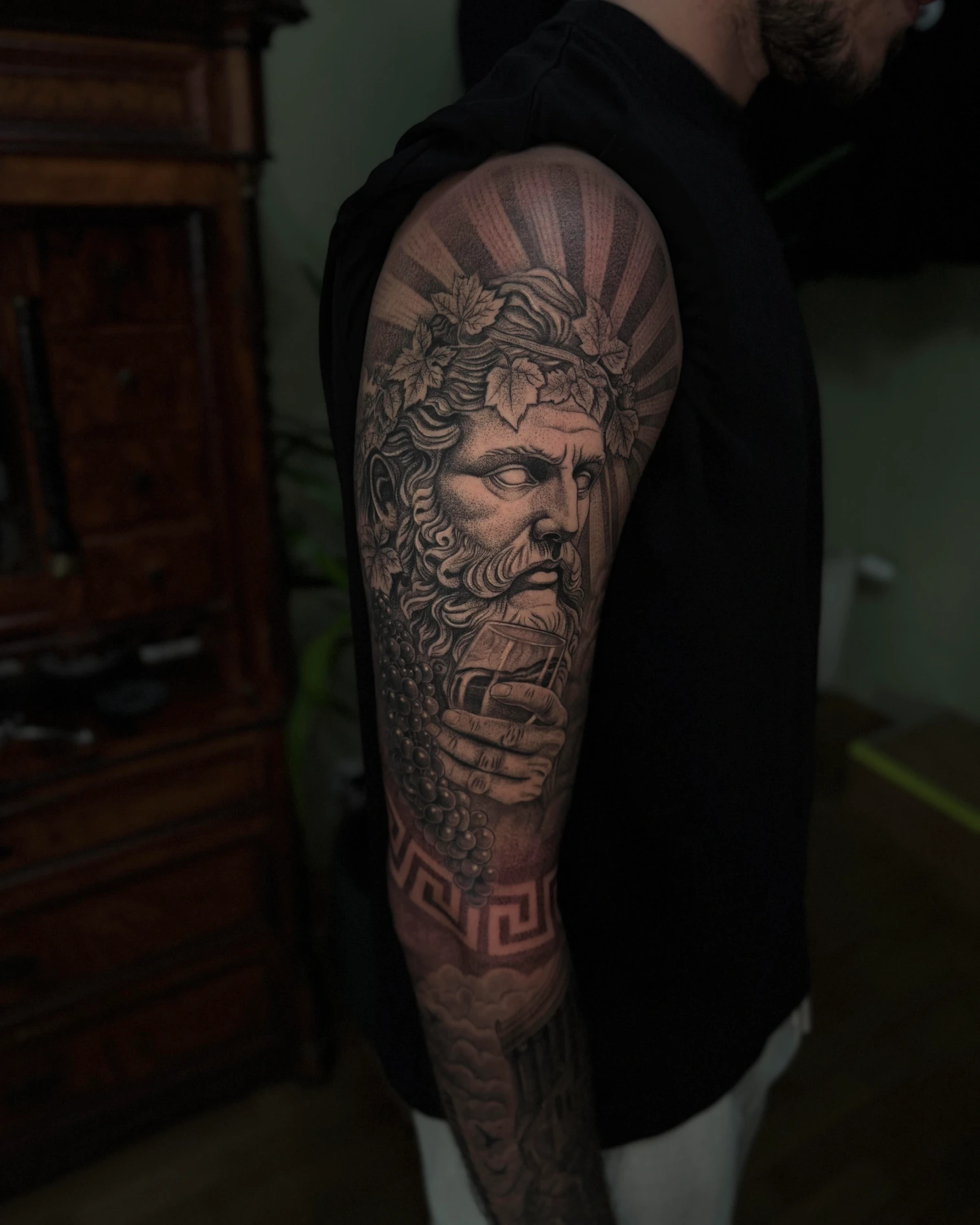 Black-and-Grey-Tattoo-Sleeve mit bärtigem Porträt, Weinlaub, Trauben und Mäandermuster