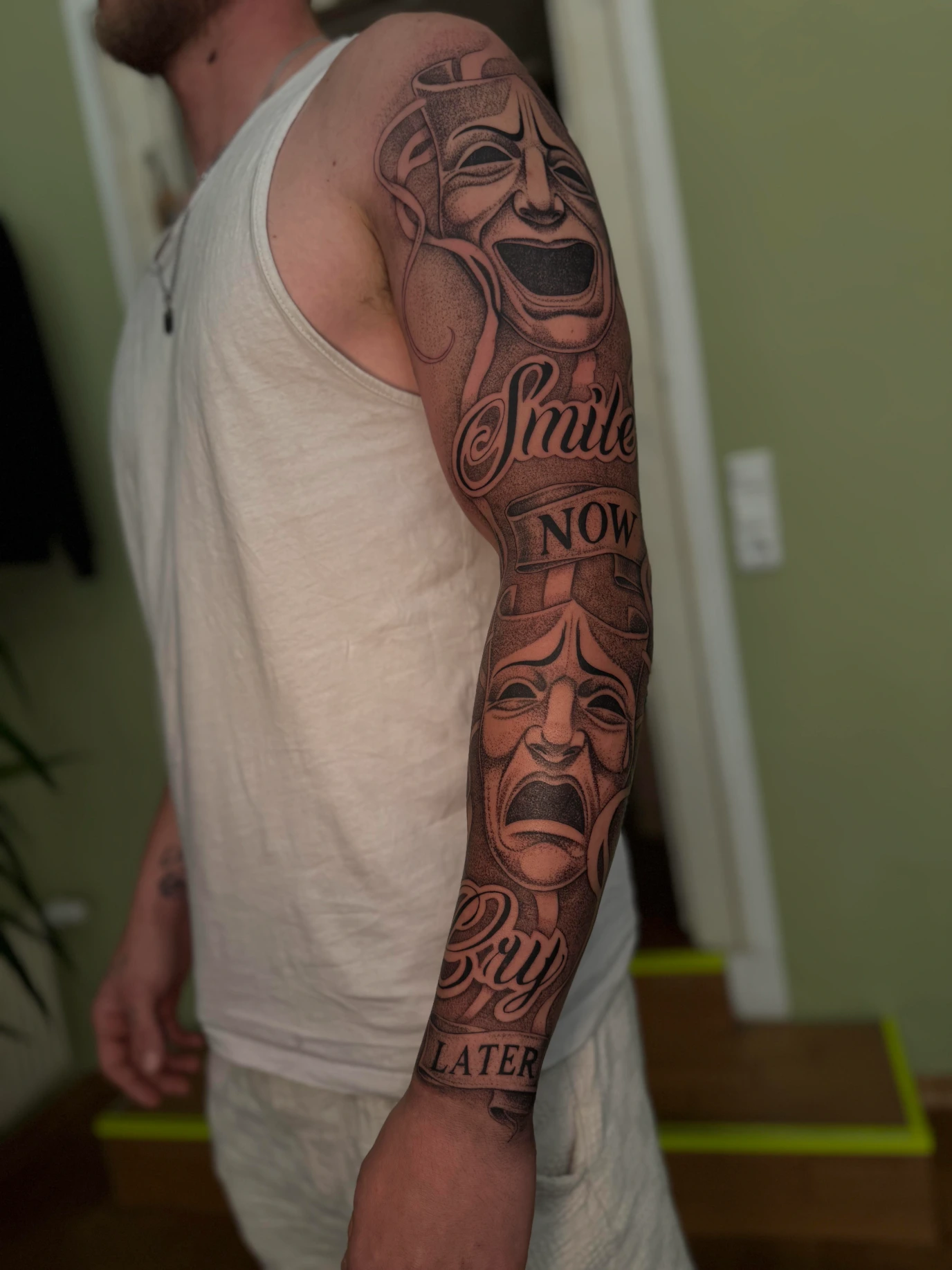 Tattoo-Sleeve mit lachender und weinender Theatermaske und dem Schriftzug Smile now, cry later